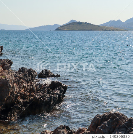Bitez Bodrum coastline scene with rocks and Aegean Sea water shimmering under summer sun, distant islands and mountains 140206880