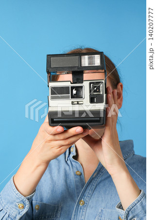 Person aims a retro camera at the viewer with blue backdrop 140207777