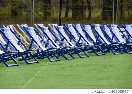 Empty blue and white deck chairs arranged in rows on green turf at an outdoor event. Sun-ready seating evokes summer vacation and holidays like Independence Day and Labor Day. Empty blue and white deck chairs arranged in rows on green turf at an outdoor event. Sun-ready seating evokes summer vacation and holidays like Independence Day and Labor Day. 140208947