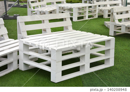 White wooden pallet benches and table arranged on a green lawn for outdoor gatherings. Rustic pallet seating set up on turf for summer parties, weddings and Easter celebrations. White wooden pallet benches and table arranged on a green lawn for outdoor gatherings. Rustic pallet seating set up on turf for summer parties, weddings and Easter celebrations. 140208948