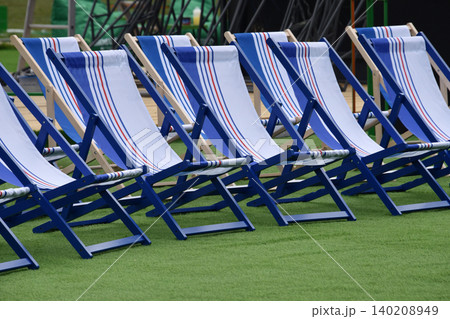 Empty blue and white deck chairs arranged in rows on green turf at an outdoor event. Sun-ready seating evokes summer vacation and holidays like Independence Day and Labor Day. Empty blue and white deck chairs arranged in rows on green turf at an outdoor event. Sun-ready seating evokes summer vacation and holidays like Independence Day and Labor Day. 140208949