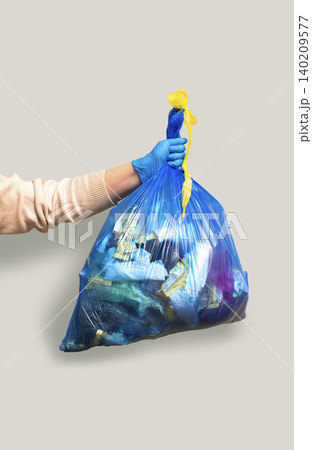 Hand holding full garbage bag on grey background isolated. Vertical high quality image Hand holding full garbage bag on grey background isolated. Vertical high quality image 140209577