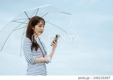 傘を持つ女性、スマホ操作 140210367