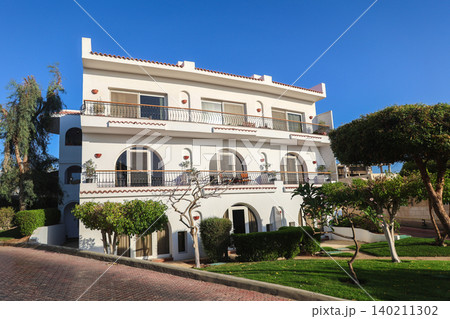Modern residential apartment building surrounded by palm trees in an Arab country under clear blue sky 140211302