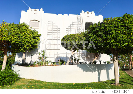 Modern residential apartment building surrounded by palm trees in an Arab country under clear blue sky 140211304