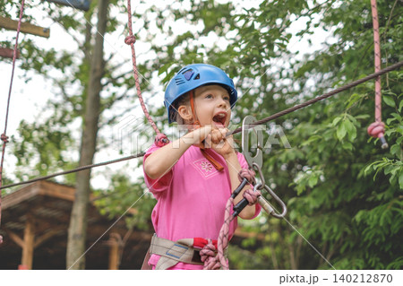 A happy, screaming child runs an obstacle course at a height, holding onto a suspended safety rope with his hands A happy, screaming child runs an obstacle course at a height, holding onto a suspended safety rope with his hands 140212870