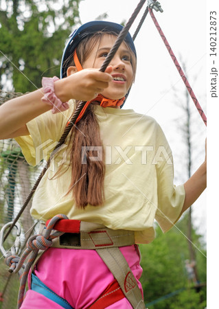 A happy girl in a protective helmet holds on to a safety rope while passing an obstacle course in a sports game 140212873