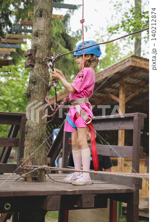 The child attaches the carbine to the safety rope while standing on the bridge. Rope town with an obstacle course in an amusement park in the forest The child attaches the carbine to the safety rope while standing on the bridge. Rope town with an obstacle course in an amusement park in the forest 140212874