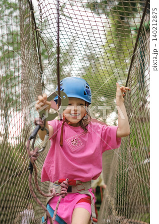 The child moves the carbine along the safety rope passing through the grid on the obstacle course. Sports summer entertainment camp for children 140212875