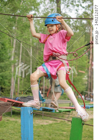 A girl in a safety helmet with a safety belt and a carabiner on a rope walks across a suspension bridge, barely passing an obstacle A girl in a safety helmet with a safety belt and a carabiner on a rope walks across a suspension bridge, barely passing an obstacle 140212877