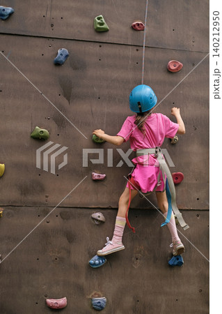A girl in pink clothes, a protective helmet with a safety rope climbs the steep wall of the climbing wall A girl in pink clothes, a protective helmet with a safety rope climbs the steep wall of the climbing wall 140212950