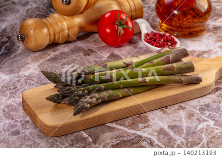 Raw asparagus spears on wooden board with tomato peppercorns and oil Raw asparagus spears on wooden board with tomato peppercorns and oil 140213193