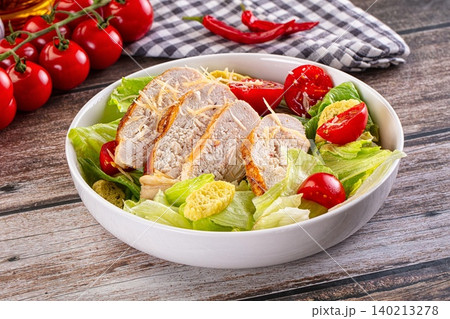Caesar salad with grilled chicken breast slices, croutons, and cherry tomatoes in white bowl 140213278