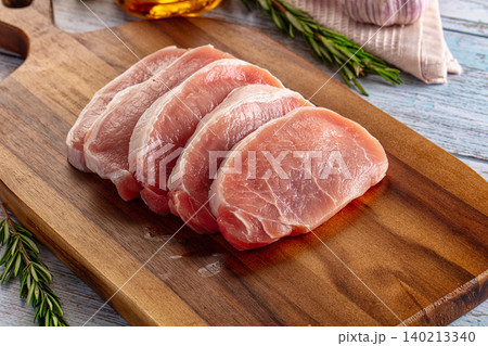 Raw pork chops arranged on wooden cutting board with fresh rosemary and garlic 140213340