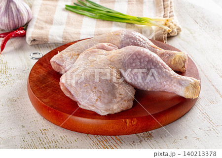 Raw whole chicken legs on wooden cutting board with garlic and spring onions 140213378