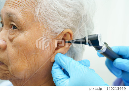 Otolaryngologist or ENT physician doctor examining senior patient ear with otoscope, hearing loss problem. 140213469