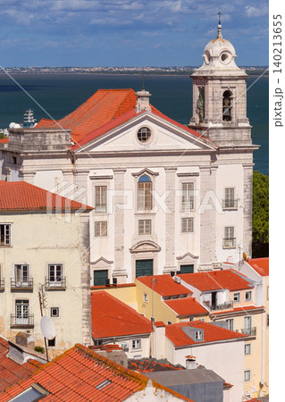 Church of Santo Estevao rises above the red tiled rooftops of Alfama with the Tagus River visible in the background on a bright day. Church of Santo Estevao rises above the red tiled rooftops of Alfama with the Tagus River visible in the background on a bright day. 140213655