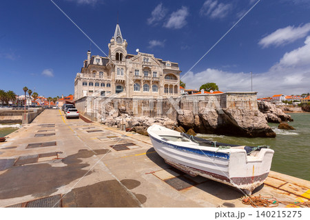 Historic waterfront villa overlooking the harbor with a traditional fishing boat moored beside the quay in Cascais, Portugal. 140215275
