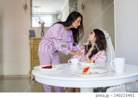 Mother and daughter. Little girl in pink pajamas with her mom eating in kitchen Mother and daughter. Little girl in pink pajamas with her mom eating in kitchen 140215491