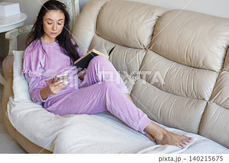 Smiling mature woman holding book and reading app notifications or news on a smartphone at home Smiling mature woman holding book and reading app notifications or news on a smartphone at home 140215675