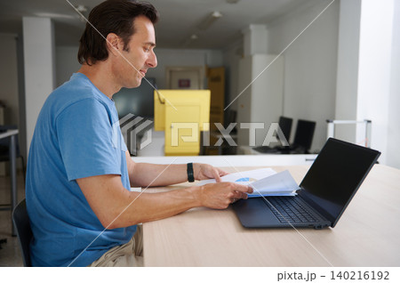 Man working at laptop and reviewing business reports at a bright office desk 140216192