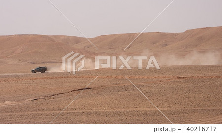 A rugged off-road vehicle drives across a vast desert landscape, leaving a long trail of dust behind it. A rugged off-road vehicle drives across a vast desert landscape, leaving a long trail of dust behind it. 140216717