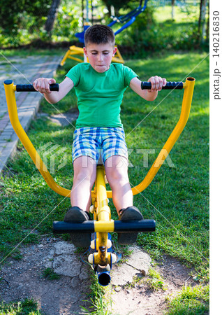 Boy exercising on outdoor fitness equipment in a park. Healthy lifestyle and outdoor activities. Boy exercising on outdoor fitness equipment in a park. Healthy lifestyle and outdoor activities. 140216830