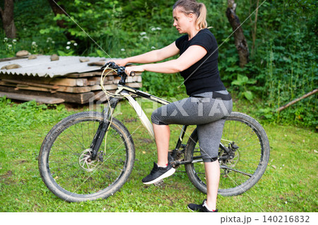 Woman preparing to ride her mountain bike outdoors on a grassy area. 140216832