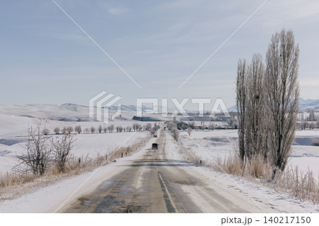Winter road through snowy countryside landscape in Kyrgyzstan with bare trees 140217150