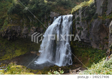 Scenic waterfall cascading into rocky pool in lush forest landscape, summer day Scenic waterfall cascading into rocky pool in lush forest landscape, summer day 140217406