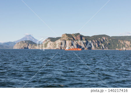 Orange ship sailing near Cape Lopatka cliffs and volcano, Kamchatka Peninsula Orange ship sailing near Cape Lopatka cliffs and volcano, Kamchatka Peninsula 140217416
