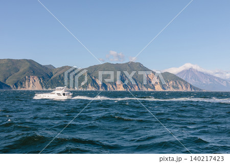 Motor yacht cruising on rough sea near Kamchatka coastline with volcano view Motor yacht cruising on rough sea near Kamchatka coastline with volcano view 140217423