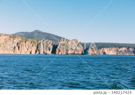 Rocky sea cliffs and coastal mountains on the Kamchatka Peninsula at summer day Rocky sea cliffs and coastal mountains on the Kamchatka Peninsula at summer day 140217424
