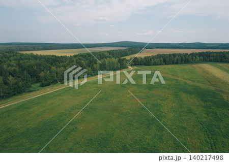 Aerial view of green meadow and forest edge with rural dirt road in summer Aerial view of green meadow and forest edge with rural dirt road in summer 140217498