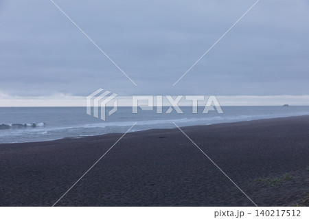 Moody overcast seascape with black sand beach and gentle waves at dawn Moody overcast seascape with black sand beach and gentle waves at dawn 140217512