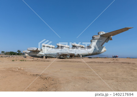 Abandoned ekranoplan ground effect aircraft on sandy shore under clear blue sky Abandoned ekranoplan ground effect aircraft on sandy shore under clear blue sky 140217694