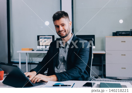 Smiling businessman in suit works on laptop in bright modern office 140218221