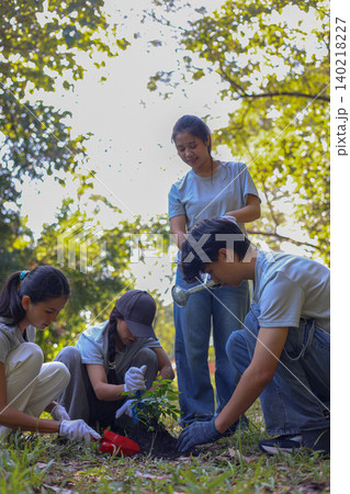 Young adults volunteer planting trees in the park for environmental conservation and sustainable future. Community service, reforestation, nature care and teamwork concept. Young adults volunteer planting trees in the park for environmental conservation and sustainable future. Community service, reforestation, nature care and teamwork concept. 140218227