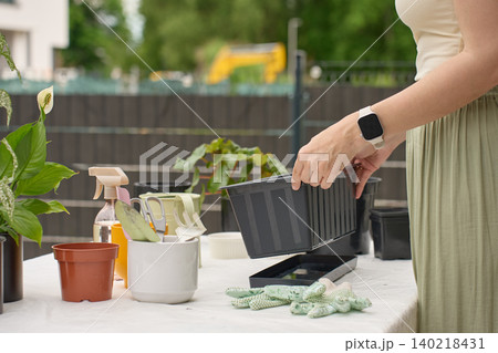 Woman prepares black planter box for outdoor gardening beside pots, gloves and hand tools Woman prepares black planter box for outdoor gardening beside pots, gloves and hand tools 140218431