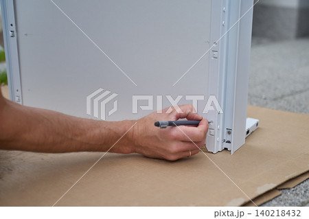 Man marks screw position with pencil on furniture panel during assembly Man marks screw position with pencil on furniture panel during assembly 140218432