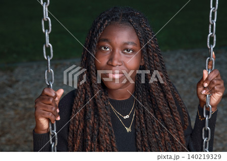 Night portrait of a calm young Black woman with long braids sitting on a playground swing Night portrait of a calm young Black woman with long braids sitting on a playground swing 140219329