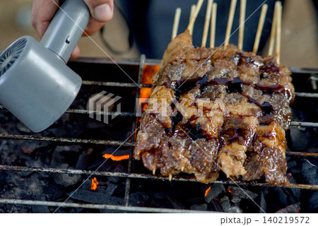 Closeup of raw meat skewers being grilled over charcoal with a culinary torch for extra char and flavor Closeup of raw meat skewers being grilled over charcoal with a culinary torch for extra char and flavor 140219572