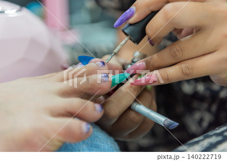 Professional nail technician applying polish during colorful manicure session featuring long acrylic nails beauty care fashion style salon services Professional nail technician applying polish during colorful manicure session featuring long acrylic nails beauty care fashion style salon services 140222719
