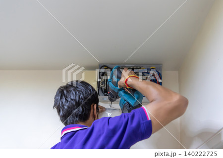 Technician using power drill while installing servicing an electrical distribution panel Indoor electrical maintenance work wiring professional tools 140222725