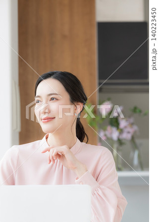 オフィスでデスクで座るパソコンの仕事をするピンクの服を顎に手を当てる考えるポーズの横顔の美人な女性	 140223450