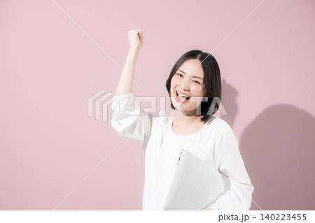 ピンク背景でノートパソコンを持つかわいい笑顔の女性社員のビジネスイメージカメラ目線 ガッツポーズ ピンク背景でノートパソコンを持つかわいい笑顔の女性社員のビジネスイメージカメラ目線 ガッツポーズ 140223455