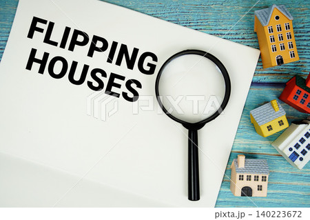 Notepad with "Flipping Houses" with magnifying glass and house model on wooden background 140223672