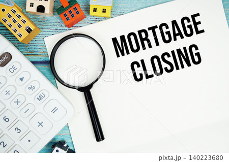 Notepad with "Mortgage Closing" with Calculator, magnifying glass and house model on wooden background 140223680