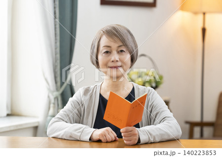 リビングで年金手帳を見るシニア女性 リビングで年金手帳を見るシニア女性 140223853