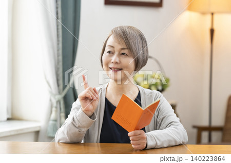 リビングで年金手帳を見るシニア女性 リビングで年金手帳を見るシニア女性 140223864